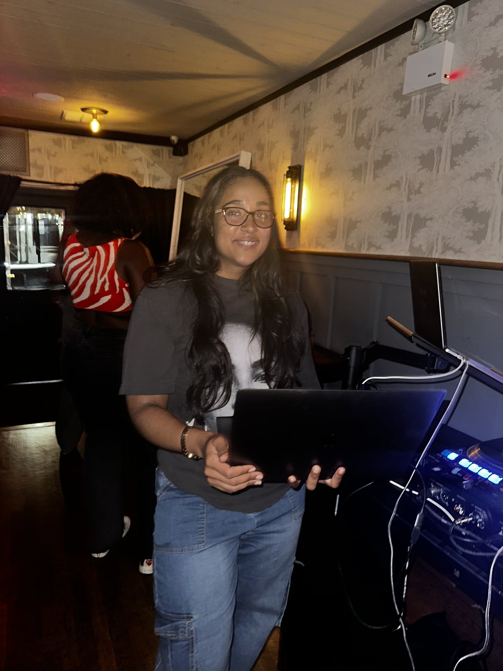 La Phiesa setting up with her laptop in hand at Woodlot, warm wall sconces lighting the booth behind her.