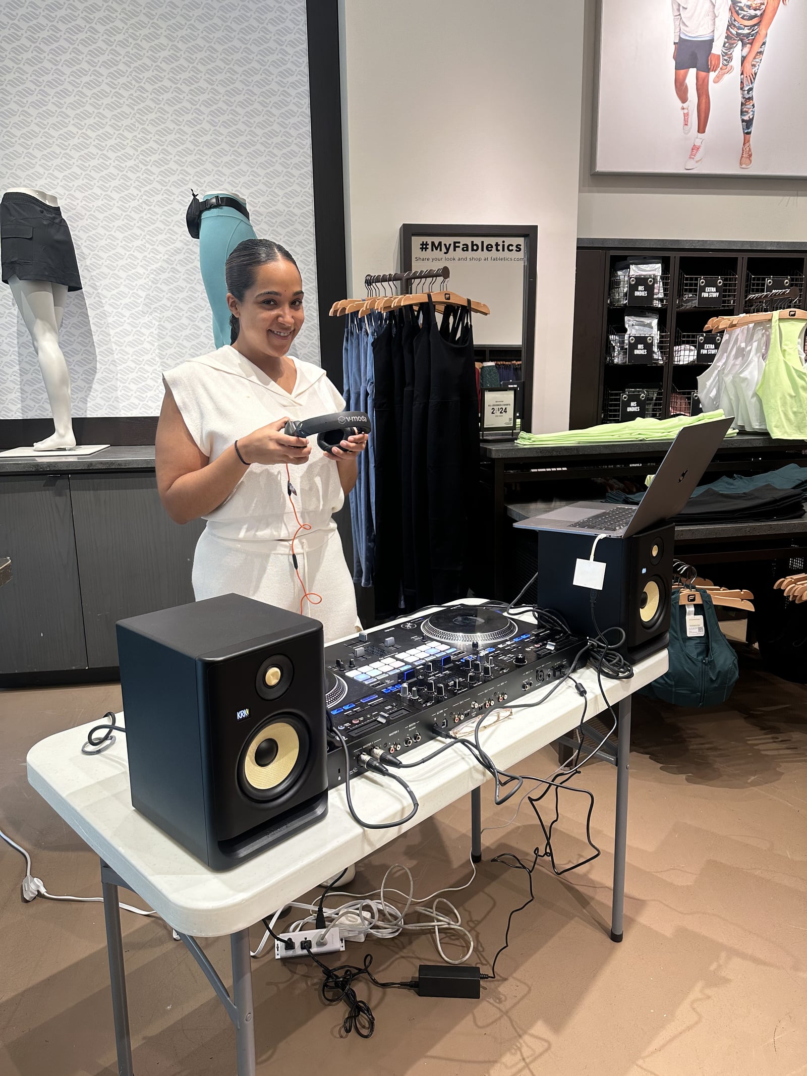 La Phiesa laughing with her headphones in hand between tracks at Fabletics, the #MyFabletics signage just over her shoulder.