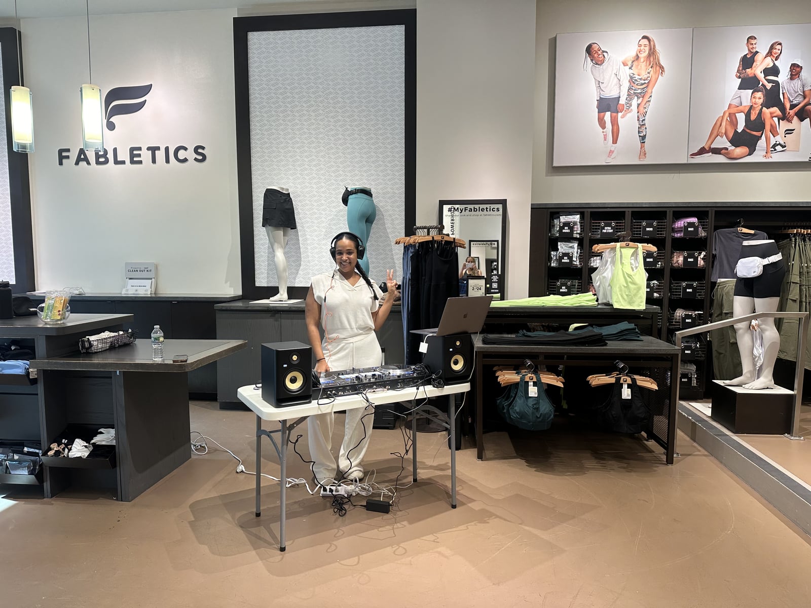 Wide view of the La Phiesa setup under the Fabletics logo wall, decks and monitors staged between the mannequins and merchandising tables.