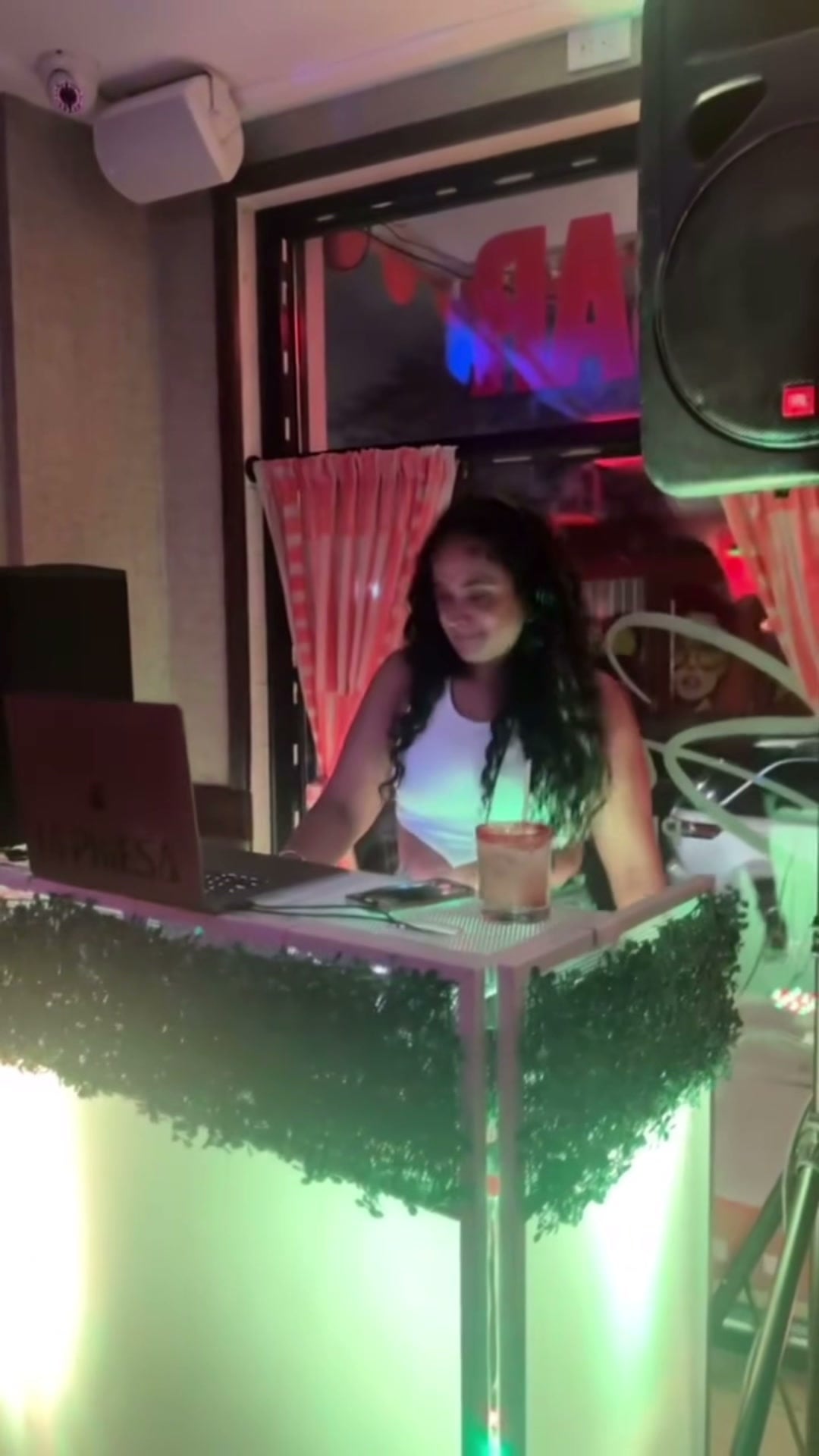 The glowing white-and-greenery DJ facade La Phiesa ran at Saucey, framed by striped curtains and the bar's street-side neon.