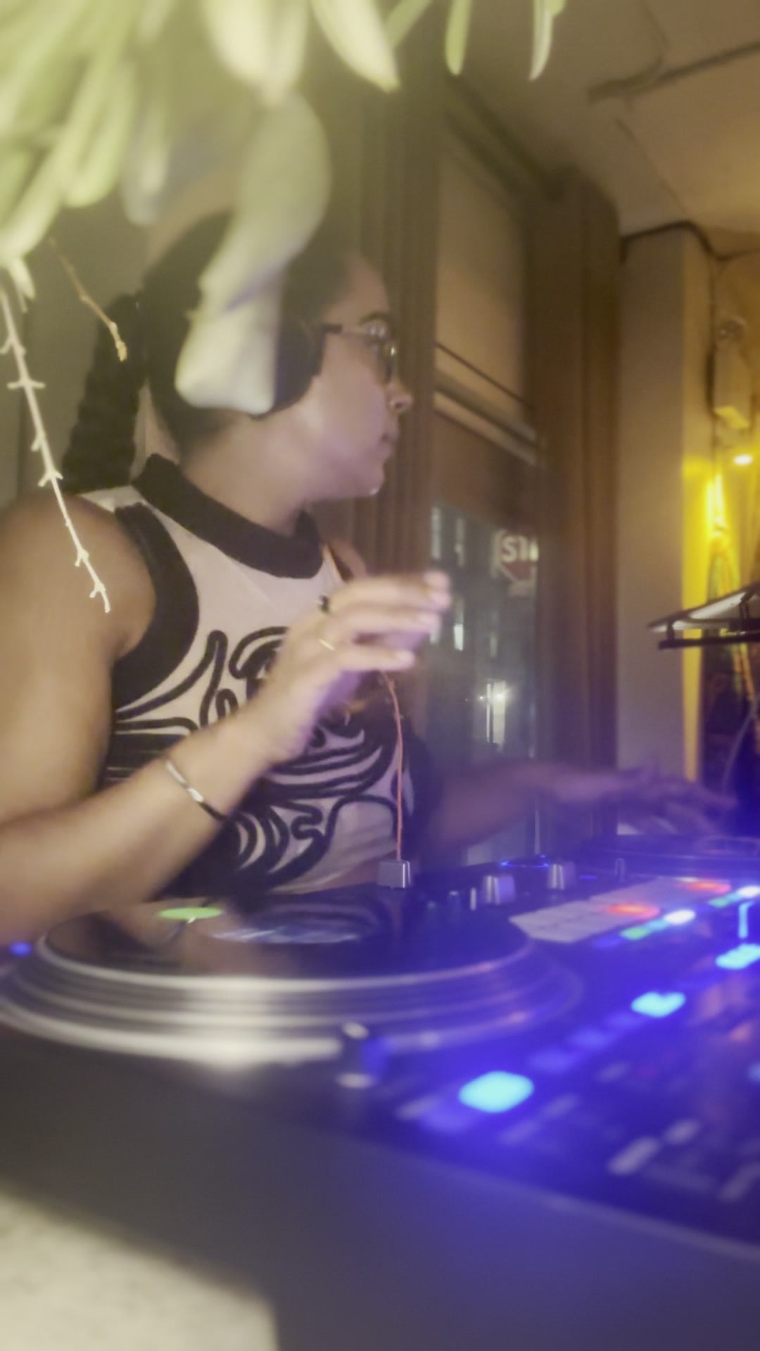 La Phiesa working the turntables in profile at PAX, the mixer glowing blue under the hanging greenery