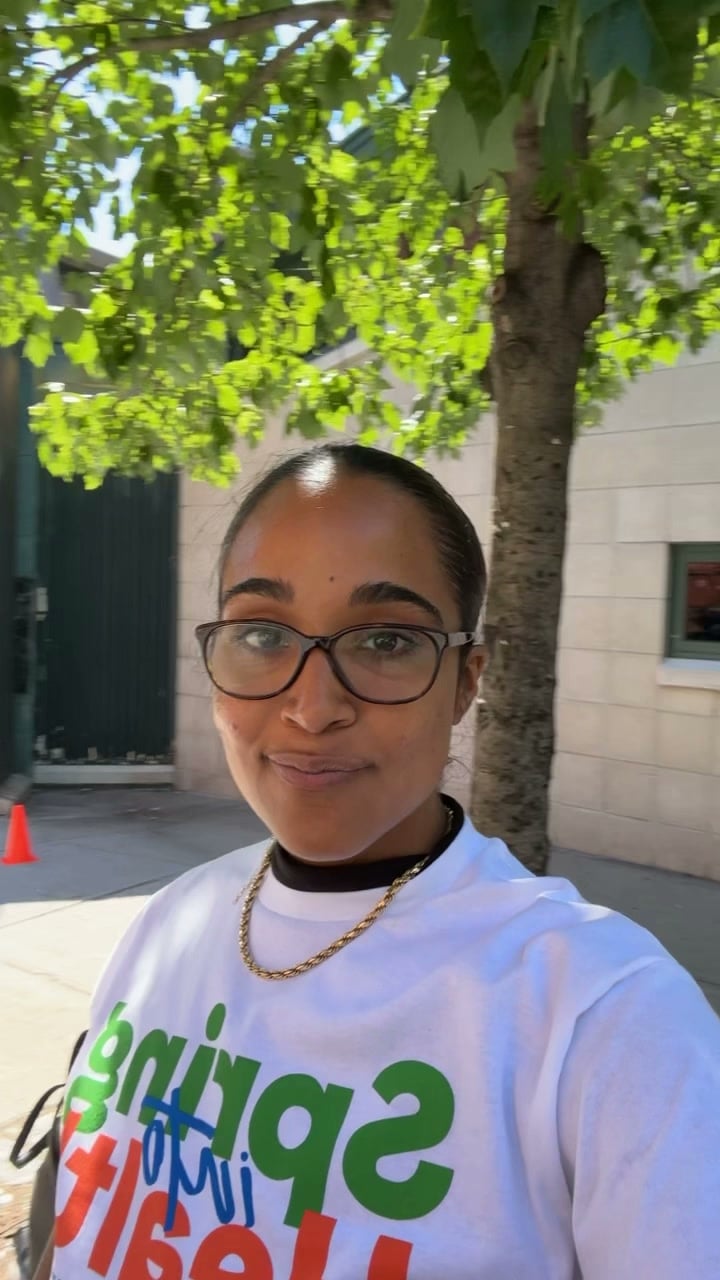 La Phiesa in the Spring into Health event tee, shaded by street trees on the block before the set