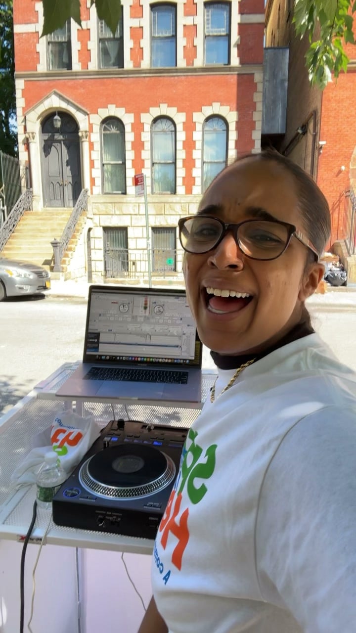 A wide grin from La Phiesa at the Spring into Health block party, brownstones lining the street behind her