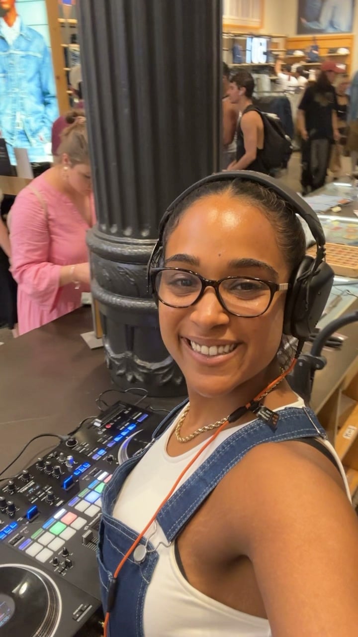 La Phiesa smiling in her headphones at the decks during the Memorial Day weekend set at the Levi's SoHo store, shoppers browsing denim behind her