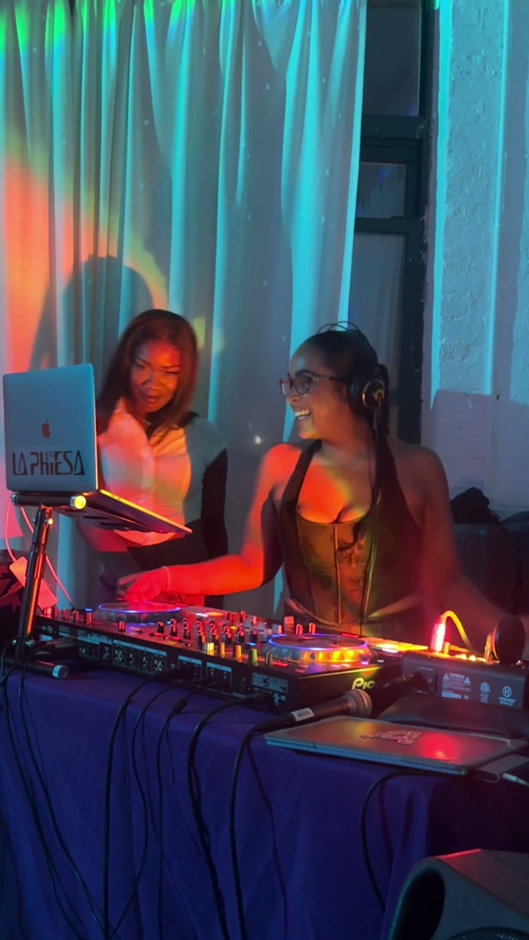 La Phiesa laughing mid-transition at Hussle Lab while a guest leans in over the booth beside her.