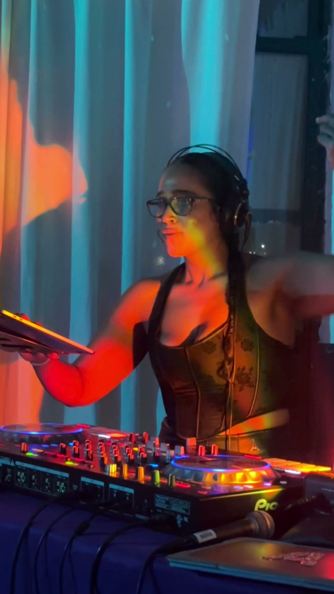 La Phiesa reaches out over the decks at Hussle Lab, one arm on the laptop and the loft lit orange and blue behind her.