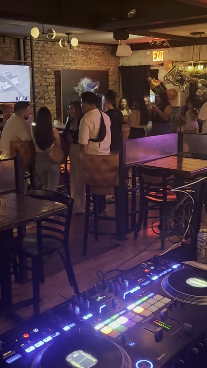 The view from La Phiesa's booth at Woodlot: turntables lit in the foreground, guests filling the brick-walled room beyond.