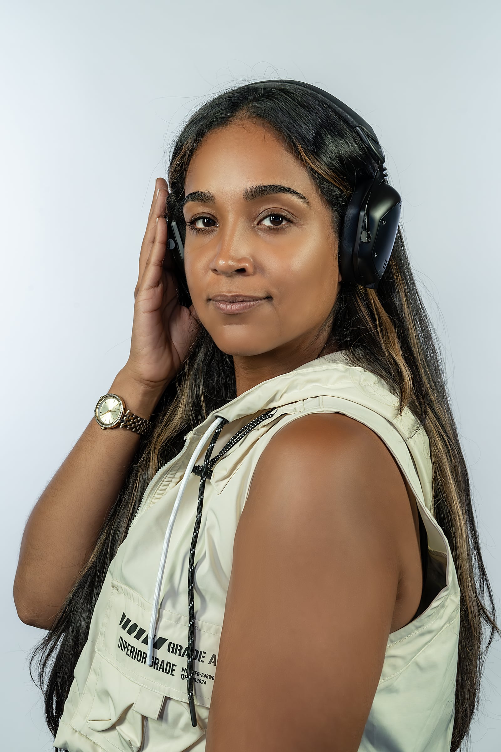 La Phiesa studio portrait, hand to her headphones in a cream utility vest
