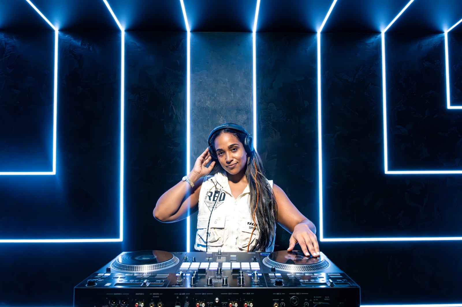 La Phiesa cueing a track, hand to her headphones, blue neon maze behind her